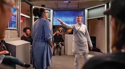 Figure 3. Audience members (seated) have an up-close view of an interaction between the whistleblower (left) and Amelia (right) in Aura’s laboratory during a performance of 
Project Amelia.